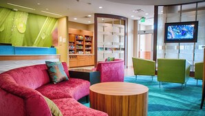 A modern lobby with a red sofa, green chairs, a wooden coffee table, and a TV on the wall.