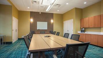 A conference room with a long table, chairs, a whiteboard, and a kitchenette area.