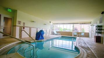 An indoor swimming pool with a tiled floor, a pool ladder, and a covered chair.