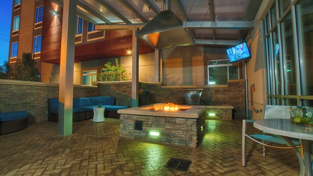An outdoor patio area with a stone fire pit, seating, and a television mounted on the wall.