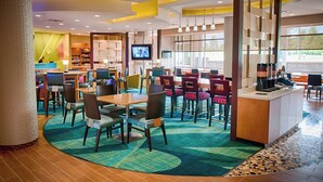 A modern hotel lobby with a central bar area, seating arrangements, and a television screen.