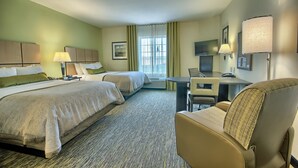 Ein Hotelzimmer mit zwei Betten, einem Schreibtisch, einem Sessel, einem Fernseher und einem Fenster mit Vorhängen.