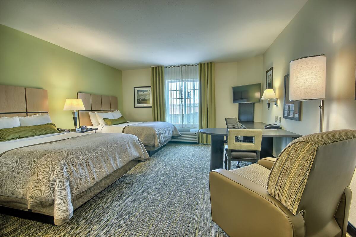 A hotel room with two beds, a desk, a chair, a TV, and a window with curtains.