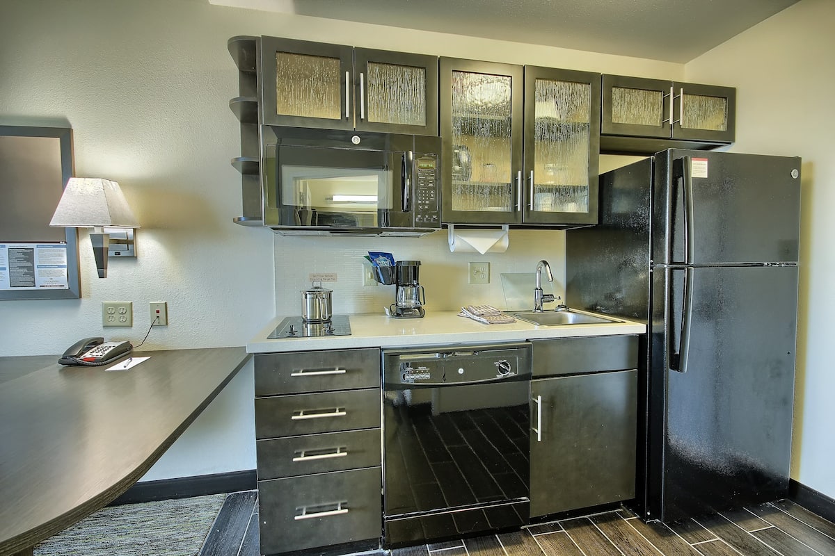 A kitchen with dark cabinets, a black refrigerator, a microwave, and a coffee maker.