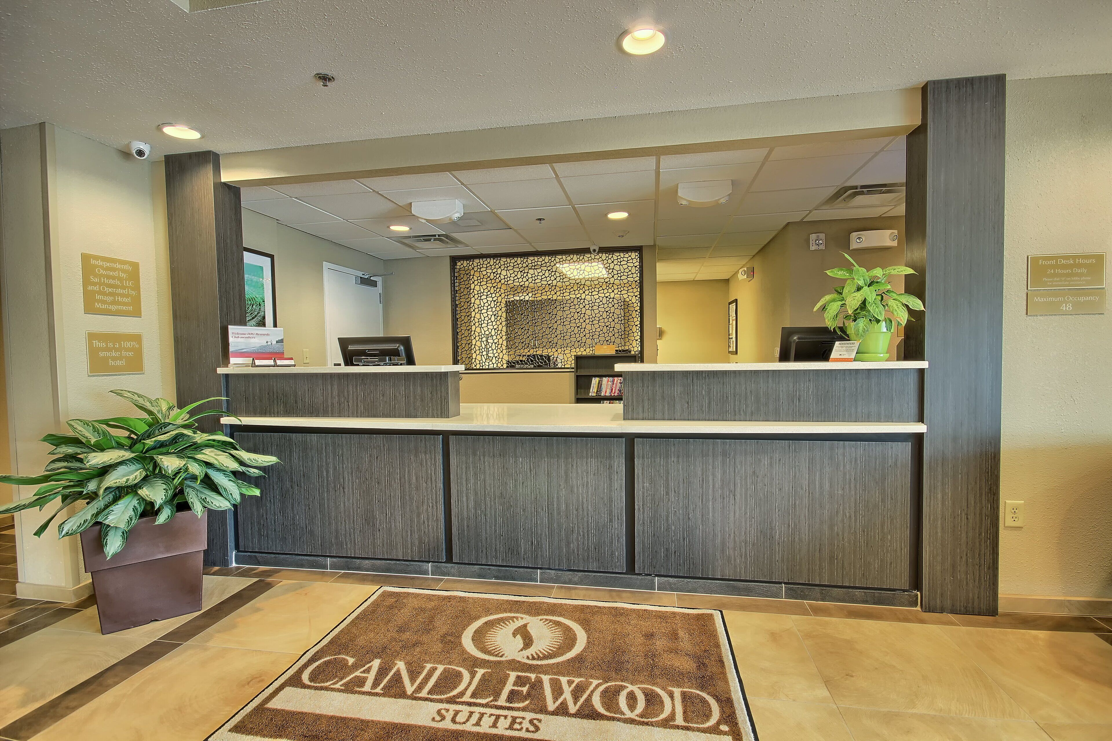 A hotel reception desk with a modern design, a welcome sign, and a plant.