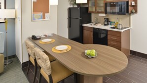 Een hotelkamer met een eettafel voor vier personen, een koelkast, een magnetron en een koffiezetapparaat.