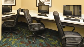 A hotel office with three computer workstations, each with a monitor, keyboard, and mouse. There are three black office chairs in front of the desks. The carpet has a multicolored pattern. - Candlewood Suites Houma by IHG (Houma)