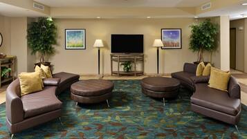 Un salón de hotel con un televisor de pantalla plana grande, dos sofás, una mesa de centro y dos plantas en macetas.