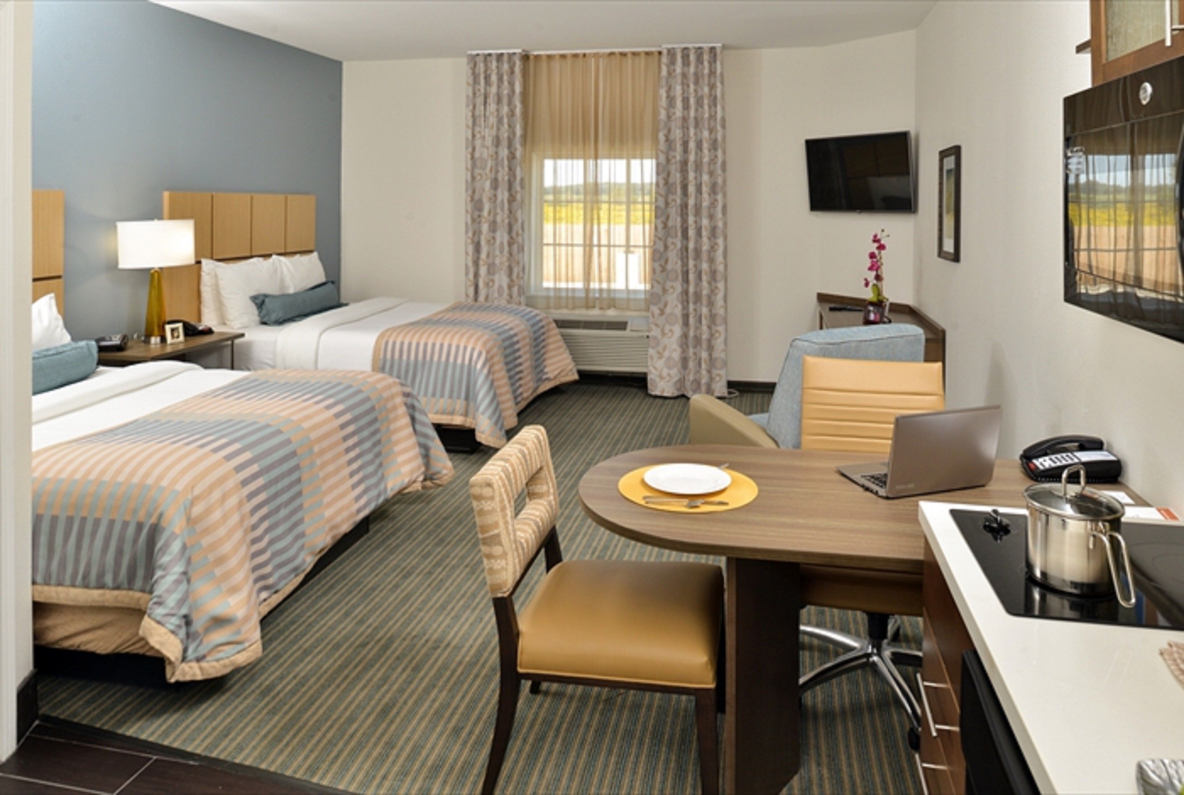 A hotel room with two beds, a desk with a laptop, a chair, a small table with a plate, a telephone, and a TV mounted on the wall.