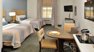 A hotel room with two beds, a desk with a laptop, a chair, a small table with a plate, a telephone, and a TV mounted on the wall.