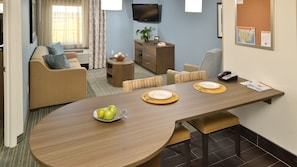 Une chambre d’hôtel moderne comprenant un coin repas, un canapé, une télévision et une petite plante.