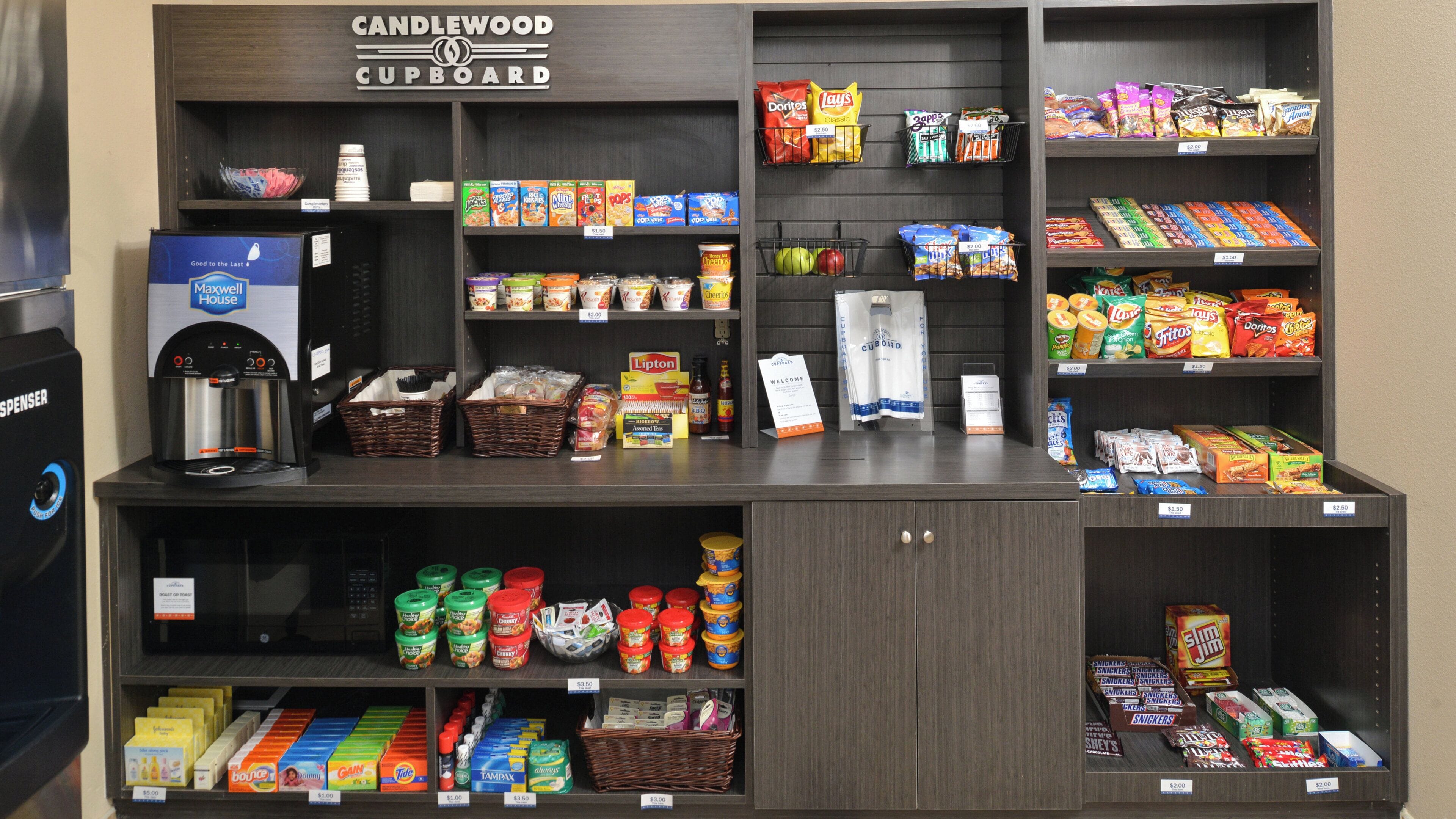 A self-serve beverage station with a coffee machine, a water dispenser, and a variety of snacks and beverages.