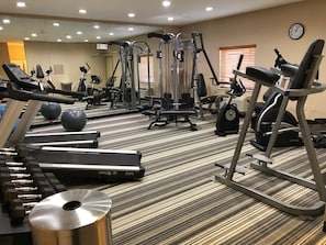 Une salle de sport équipée de divers appareils d’exercice, notamment des tapis de course, des vélos elliptiques et des poids libres.