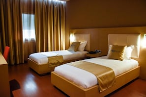 Habitación de hotel con dos camas, una mesita de noche, una lámpara y una ventana con cortinas.