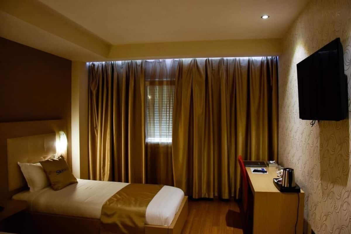 A hotel room with a bed, a desk, a chair, a television, and a window with curtains.