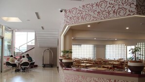 A hotel lobby with a central seating area, a staircase, and potted plants.