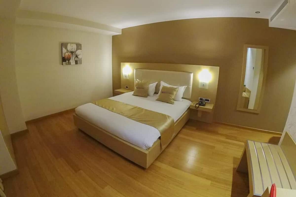 A hotel room with a large bed, bedside tables, a mirror, and a wooden floor.