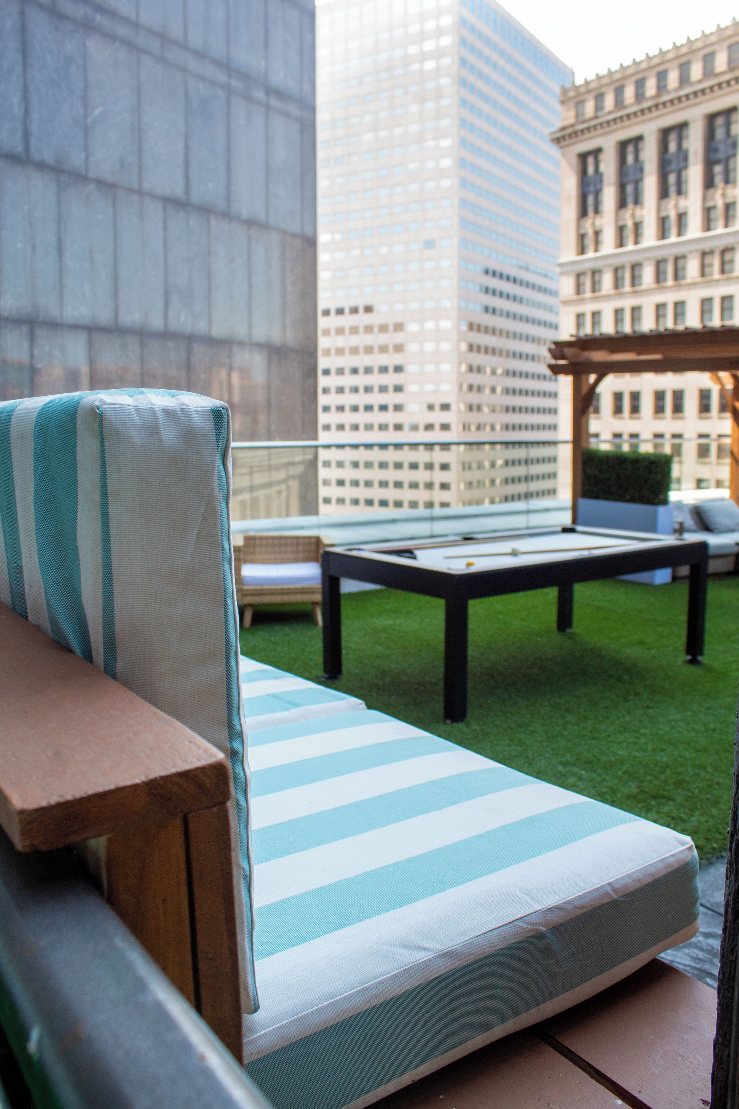 A rooftop lounge with a pool table, a cushioned seating area, and a view of tall buildings.