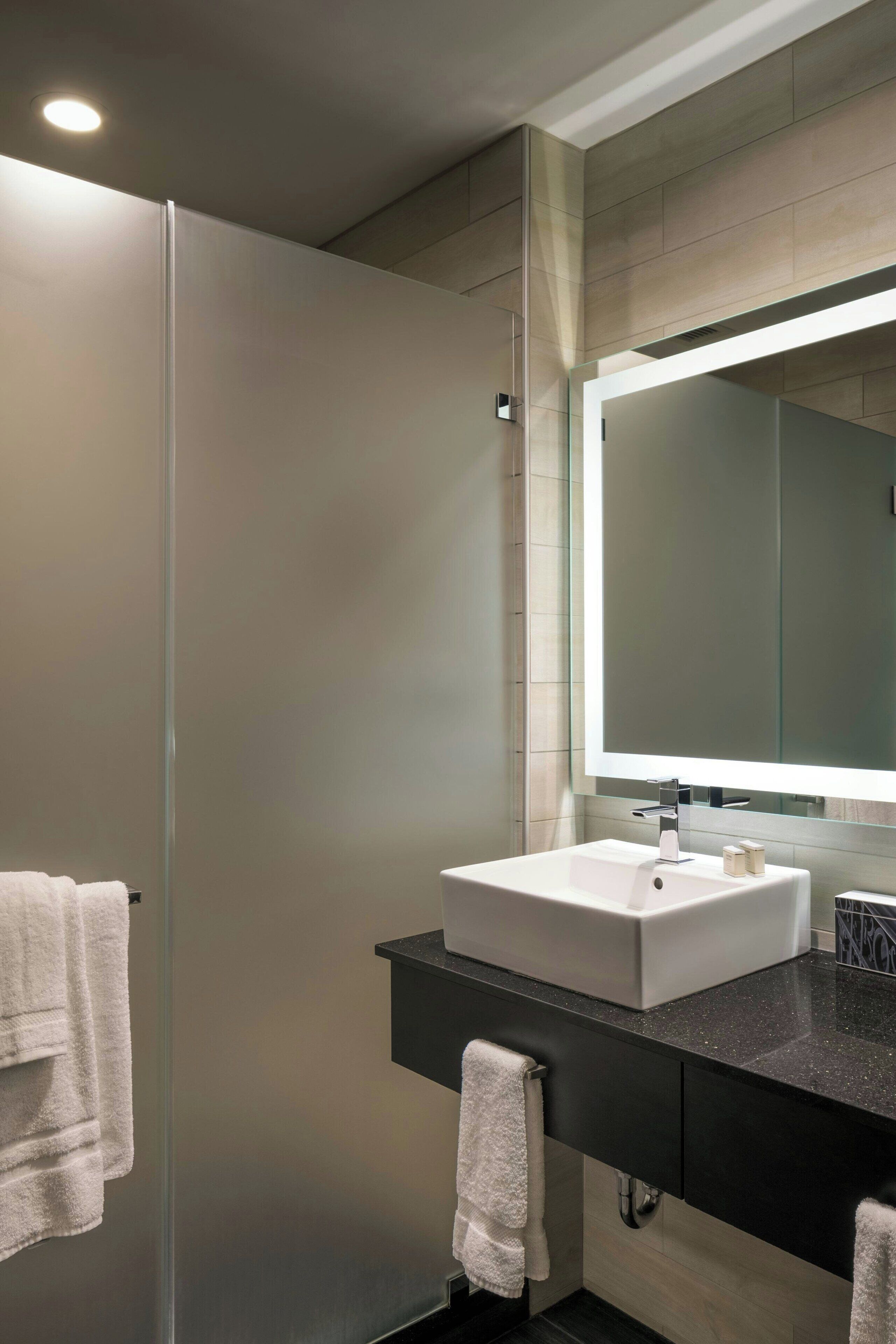 A modern bathroom with a white sink, black countertop, and a large mirror.