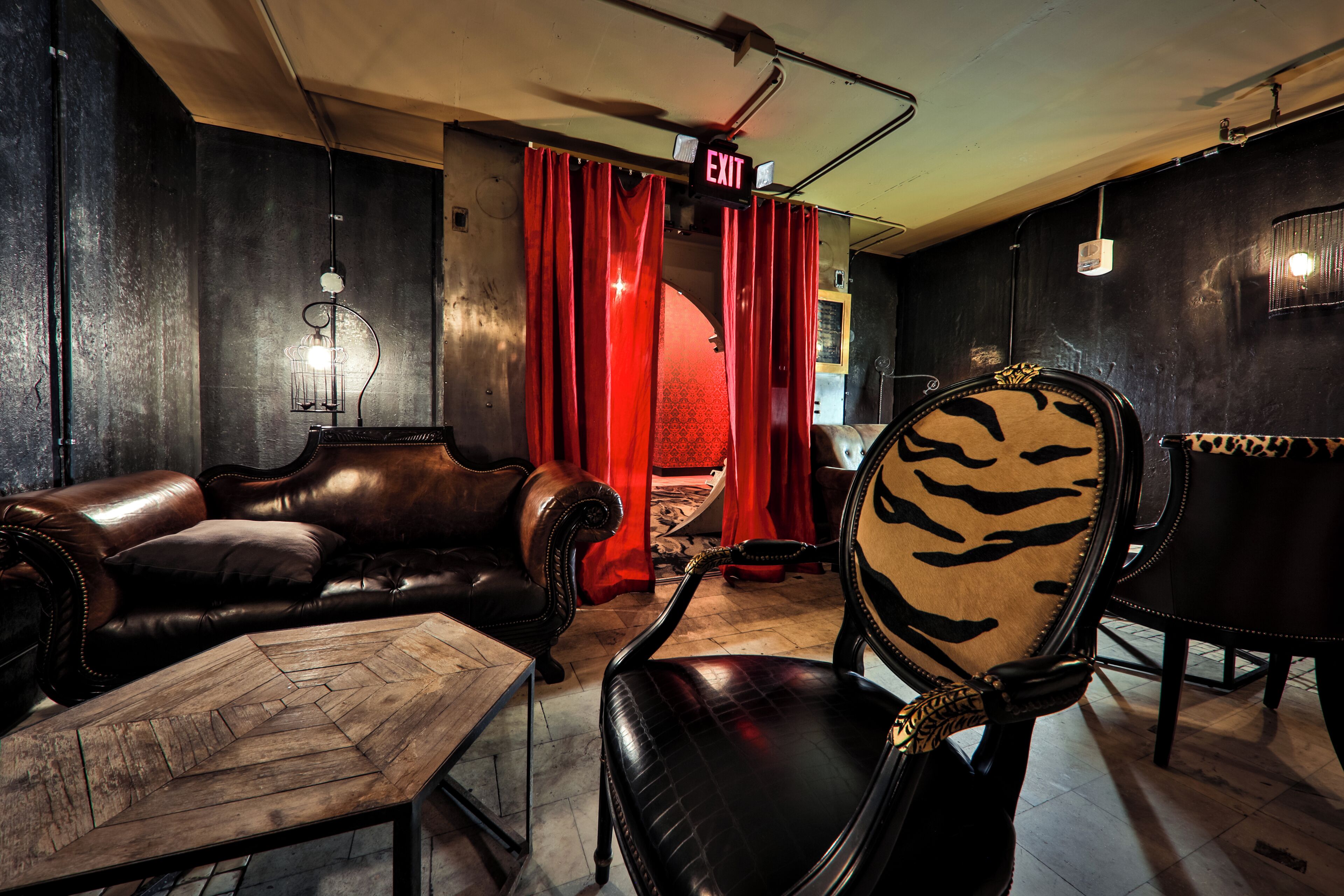 A room with a leather sofa, a patterned armchair, a wooden coffee table, and red curtains.