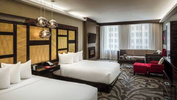 A hotel room with two beds, a sofa, a TV, and a large window with curtains.