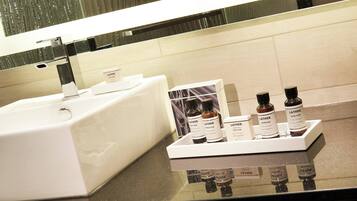 Casa de banho com lavatório branco e espelho, um tabuleiro com várias embalagens de gel de banho Lather e um dispensador de sabonete branco.