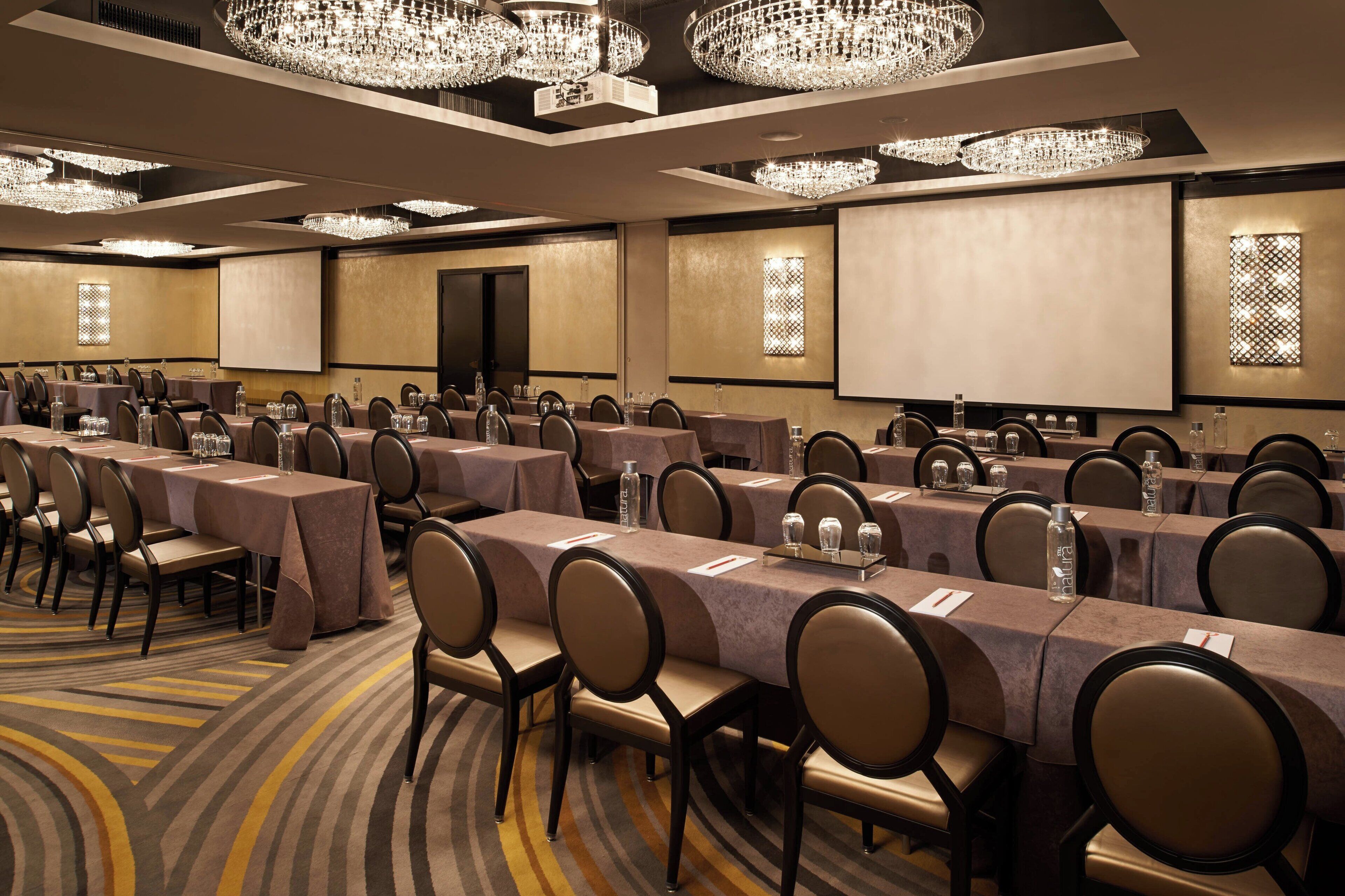 A conference room with multiple tables, chairs, and a large screen.