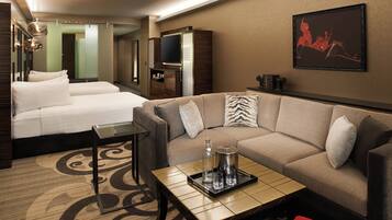Una habitación de hotel con cama, sofá, mesa de centro, televisor y un cuadro en la pared.
