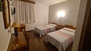 Ein Hotelzimmer mit zwei Betten, einem Schreibtisch mit Lampe, einem Spiegel und einem am Wand befestigten Fernseher.