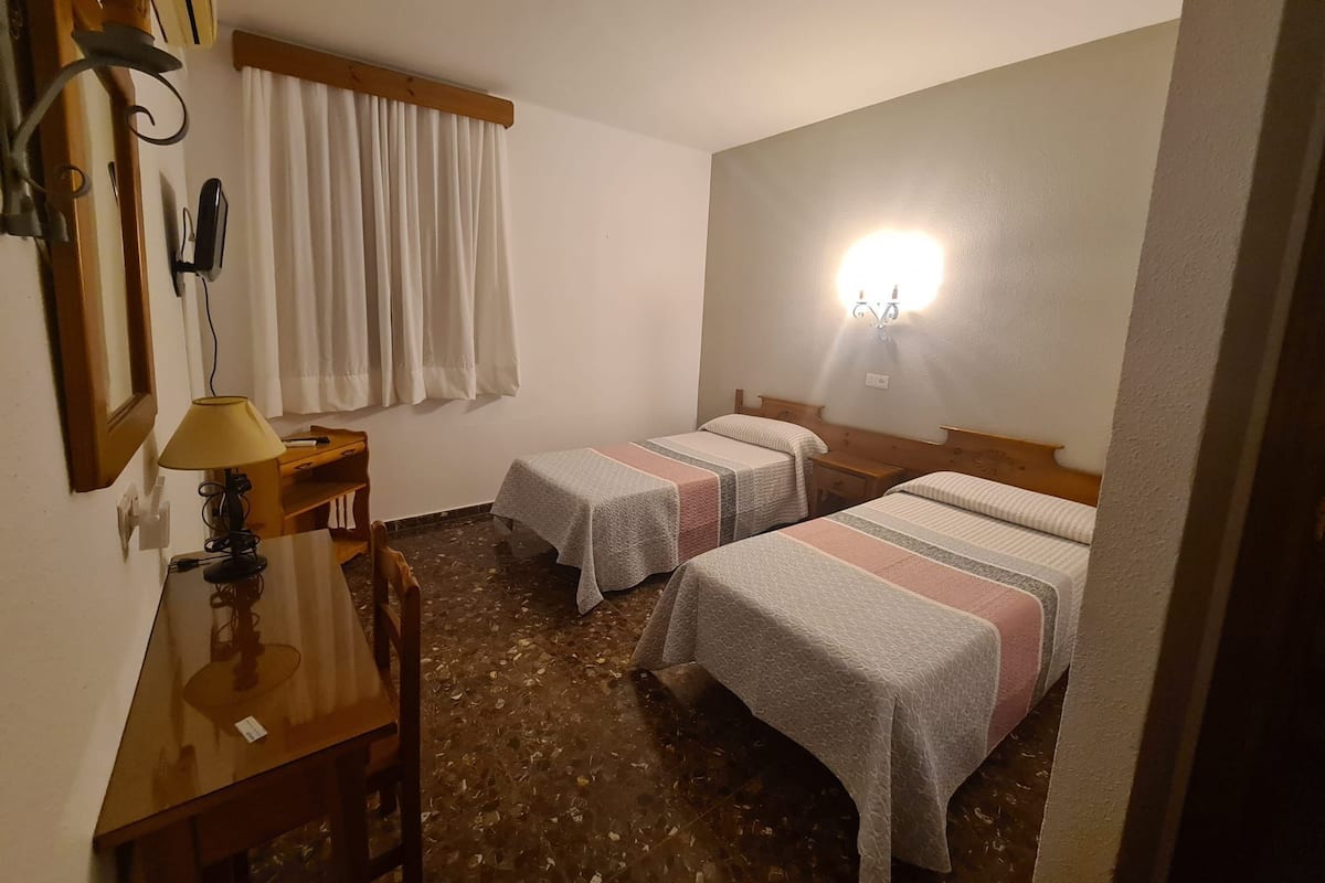 Une chambre d’hôtel avec deux lits, un bureau avec une lampe, un miroir et un téléviseur fixé au mur.