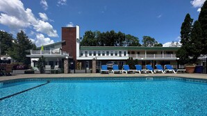 Une piscine avec des chaises longues et, au fond, un bâtiment doté d’une cheminée en briques.