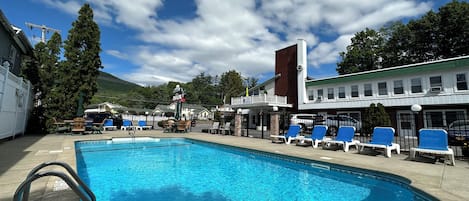 Una piscina con sillas de descanso, un área de estar techada y un edificio con techo verde.