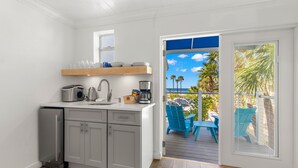 A compact kitchen with a built-in refrigerator, a coffee maker, and a wooden shelf above the sink. - Inn on the Beach - 18+ only (St. Pete Beach)