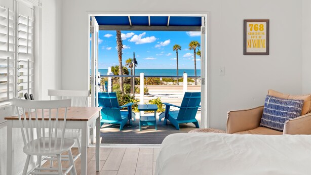A room with a view of the beach, a table with chairs, and a bed with a pillow. - Inn on the Beach - 18+ only (St. Pete Beach)
