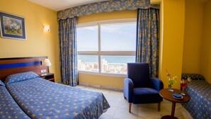 A hotel room with two beds, a chair, a small table with drinks, and a large window with curtains. - Hotel Biarritz (Gandia)