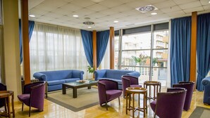 A hotel lobby with blue sofas, purple armchairs, a coffee table, and a large window with curtains. - Hotel Biarritz (Gandia)