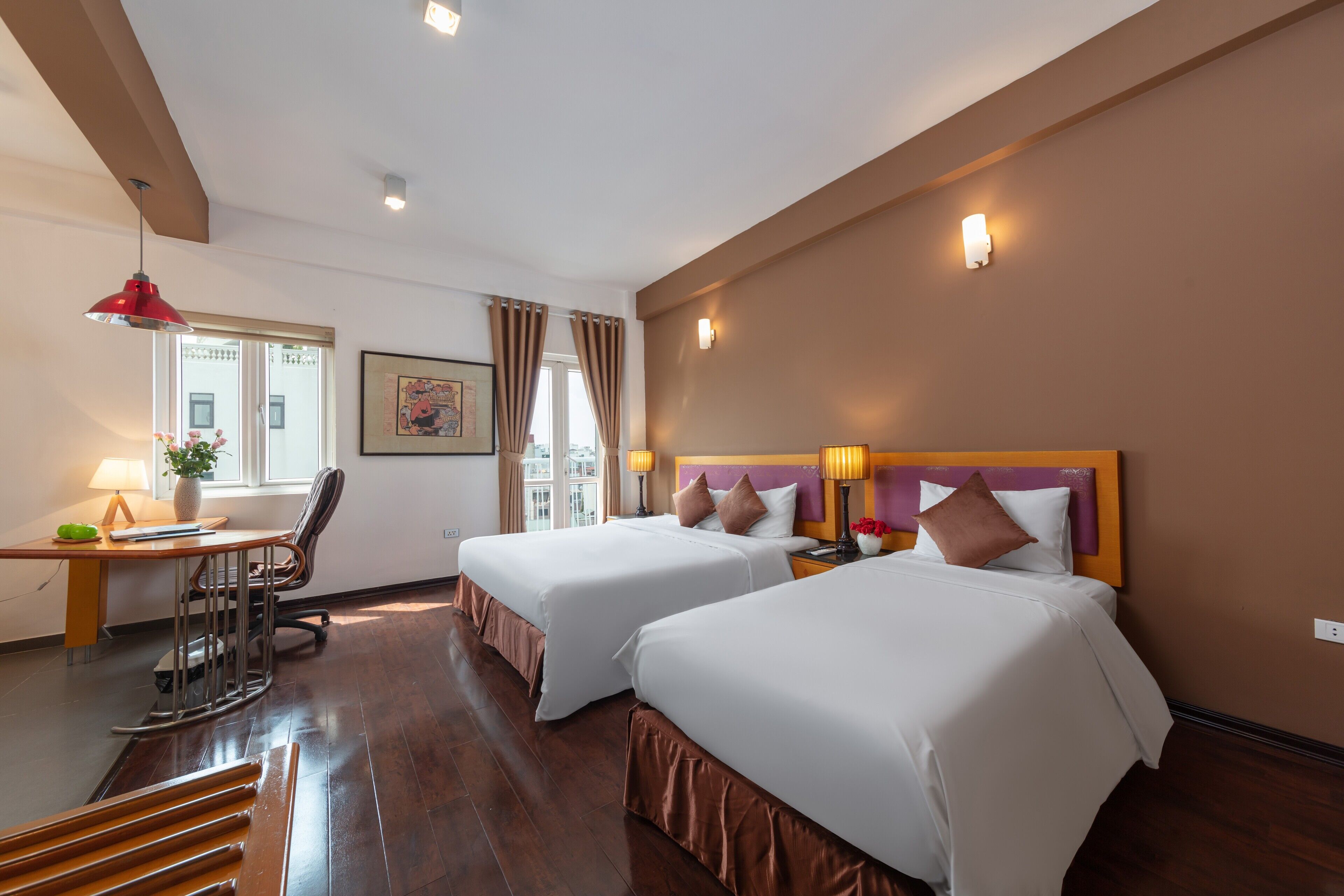Habitación de hotel con dos camas, un escritorio con silla, una ventana con cortinas y una lámpara fijada a la pared.