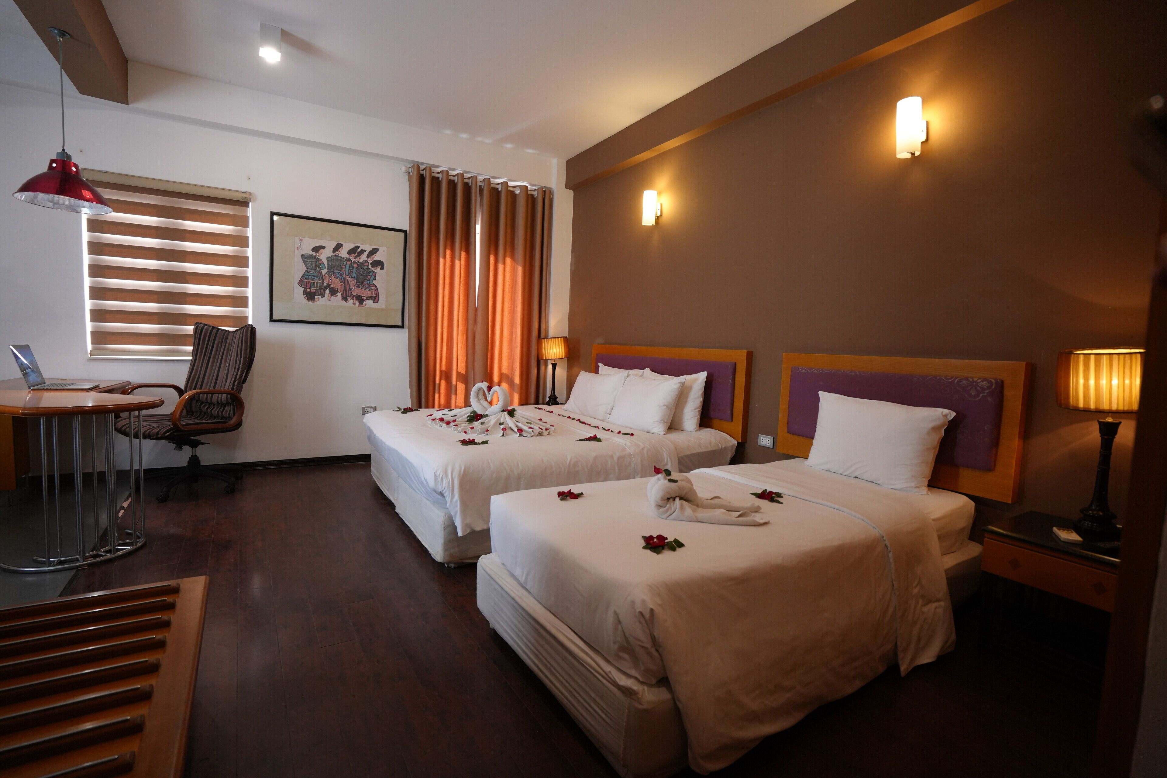 A hotel room with two beds, a desk, a chair, and a laptop.