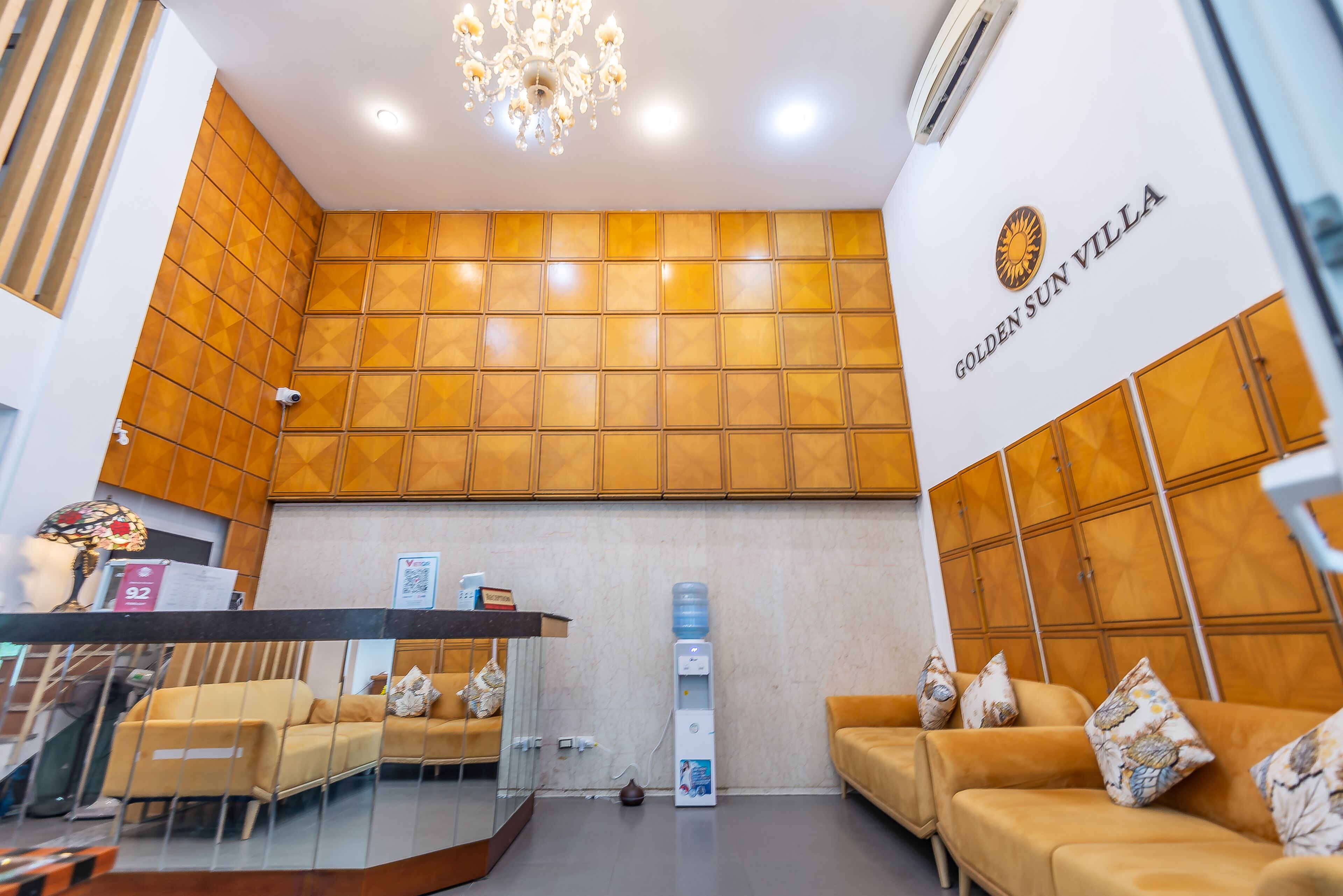 A reception area with a modern design, featuring a reception desk, two sofas, a chandelier, and a wall-mounted logo for Golden Sun Villa.