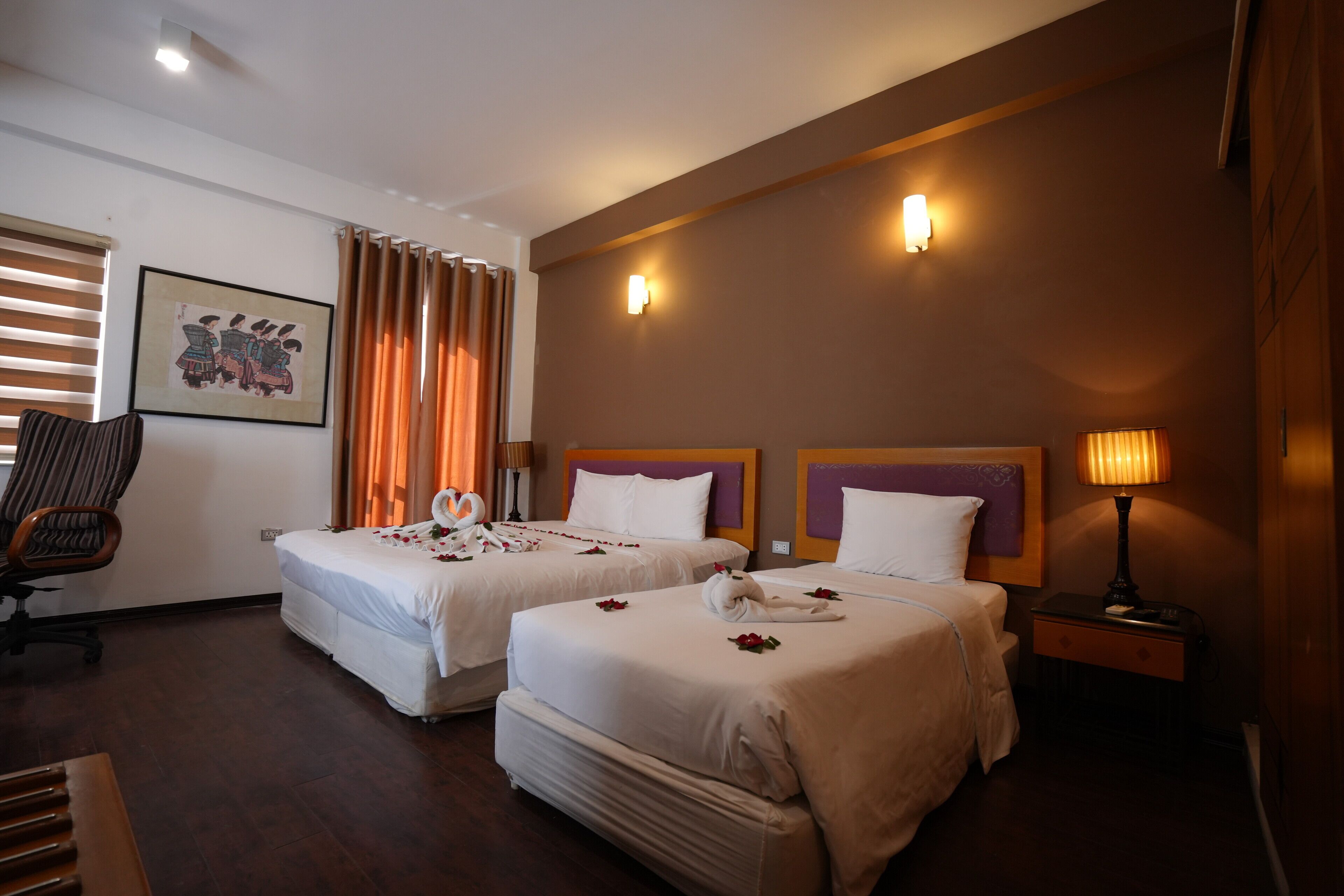 A hotel room with two beds, a chair, a desk, and a lamp.
