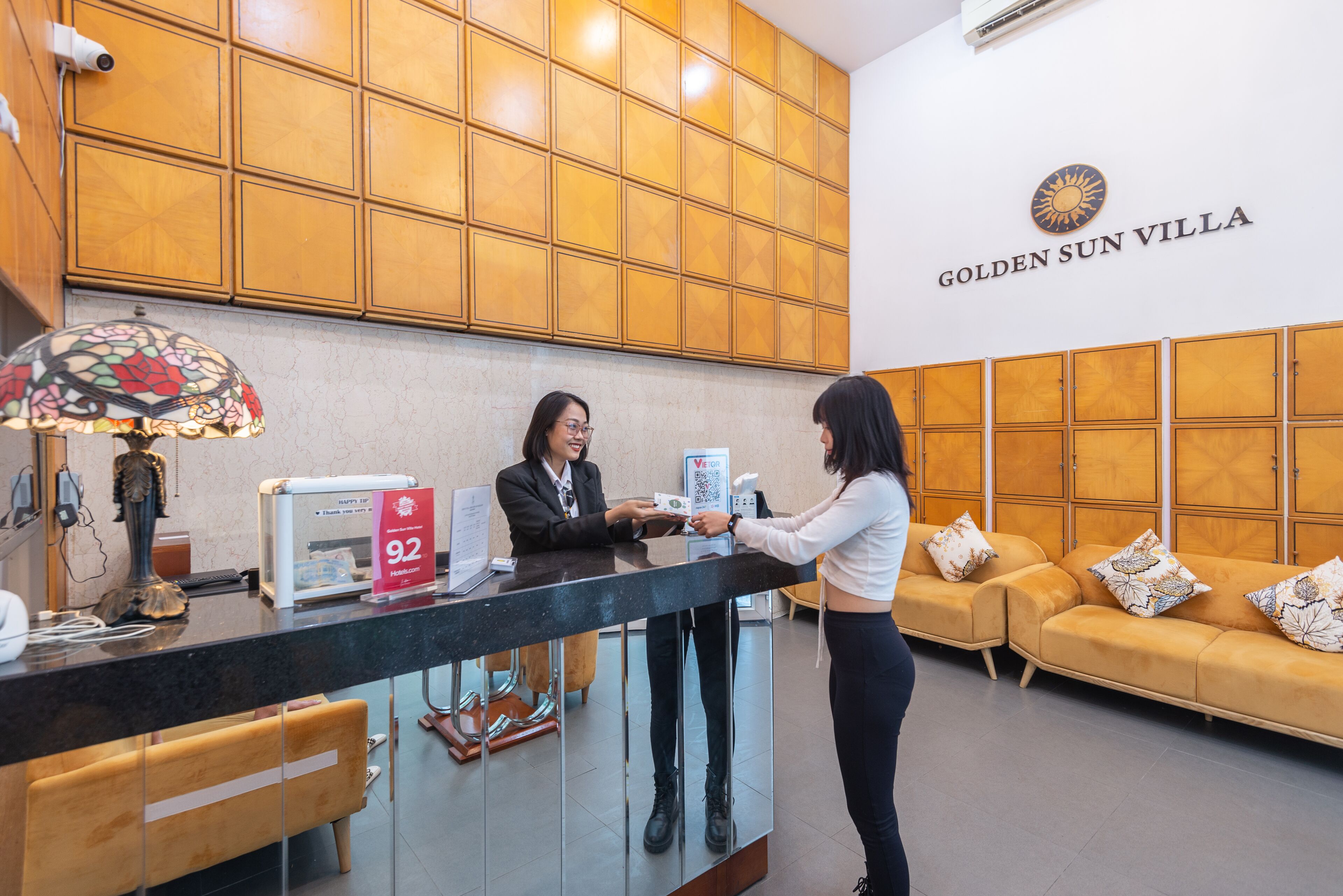 A reception desk with a receptionist, a digital screen, and a sign indicating room number 92.