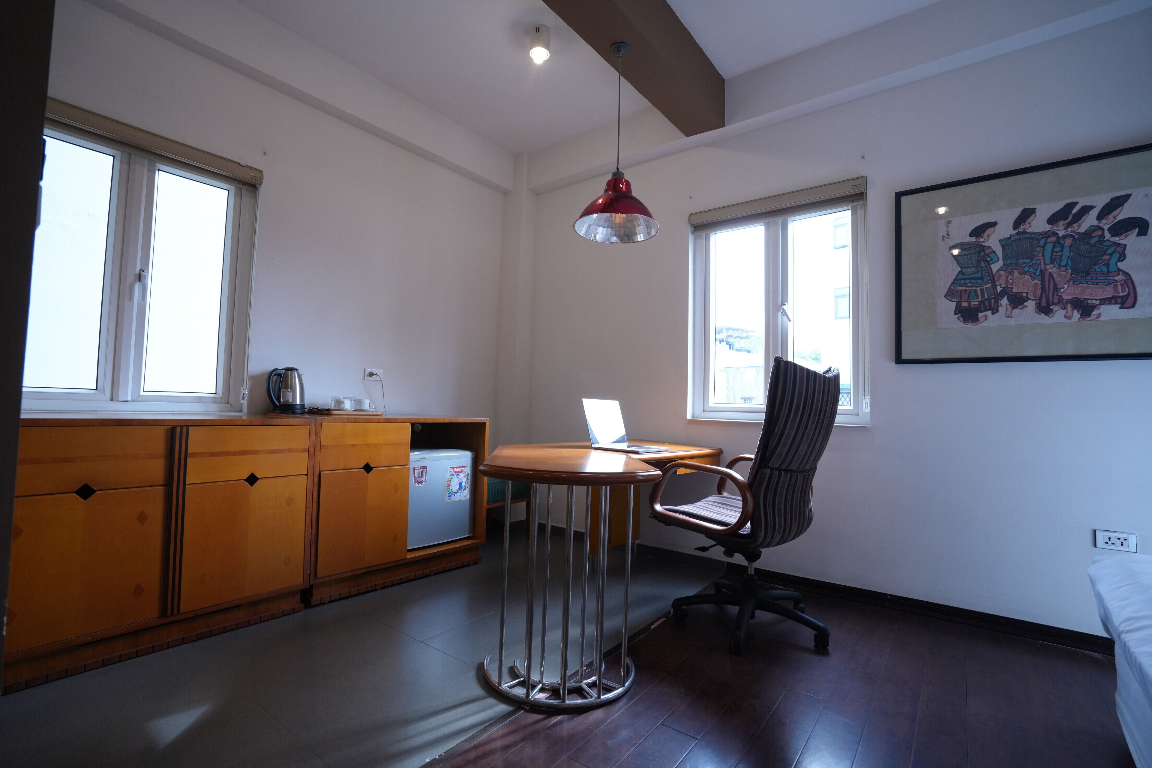 A modern kitchen with wooden cabinets, a round table, a red pendant light, and a laptop on the table.