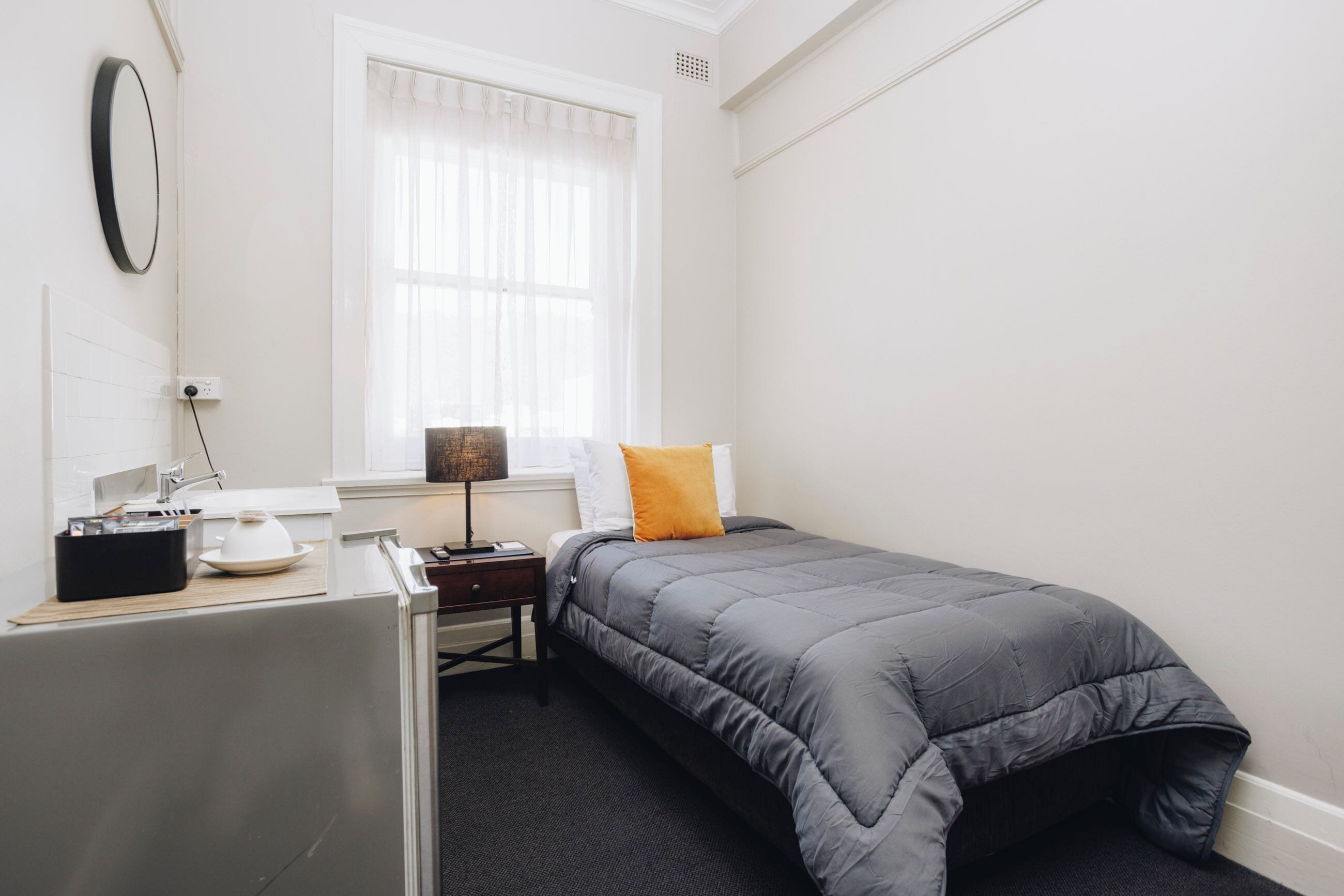 Un dormitorio con una cama, un escritorio, una lámpara y una ventana con cortinas.