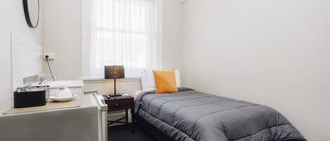 Un dormitorio con una cama, un escritorio, una lámpara y una ventana con cortinas.