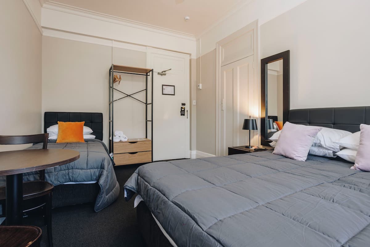 A hotel room with a bed, a desk, a chair, a wardrobe, and a mirror.