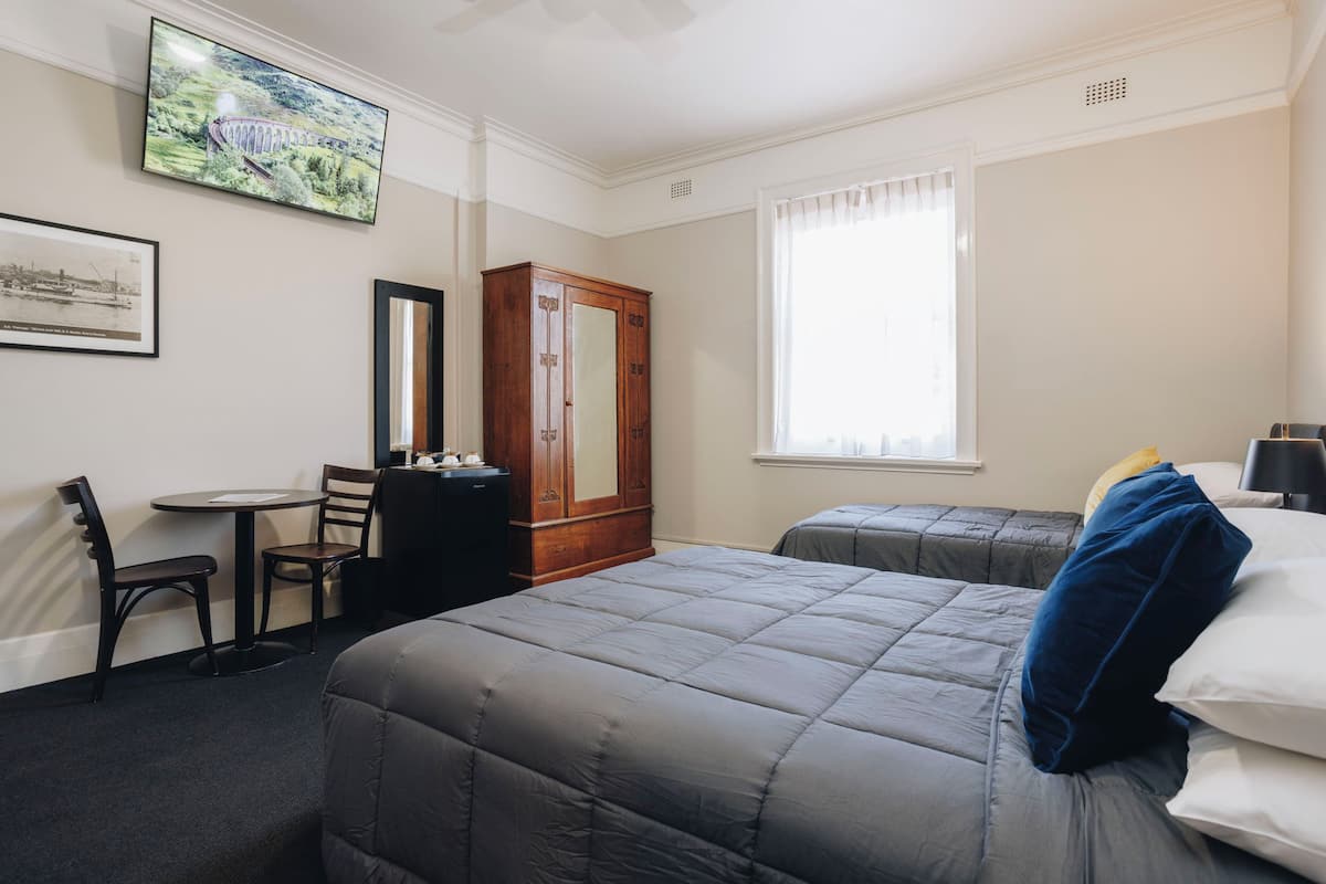A hotel room with two beds, a desk with a chair, a wardrobe, and a large window.