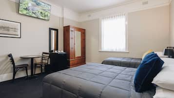 A hotel room with two beds, a desk with a chair, a wardrobe, and a large window.