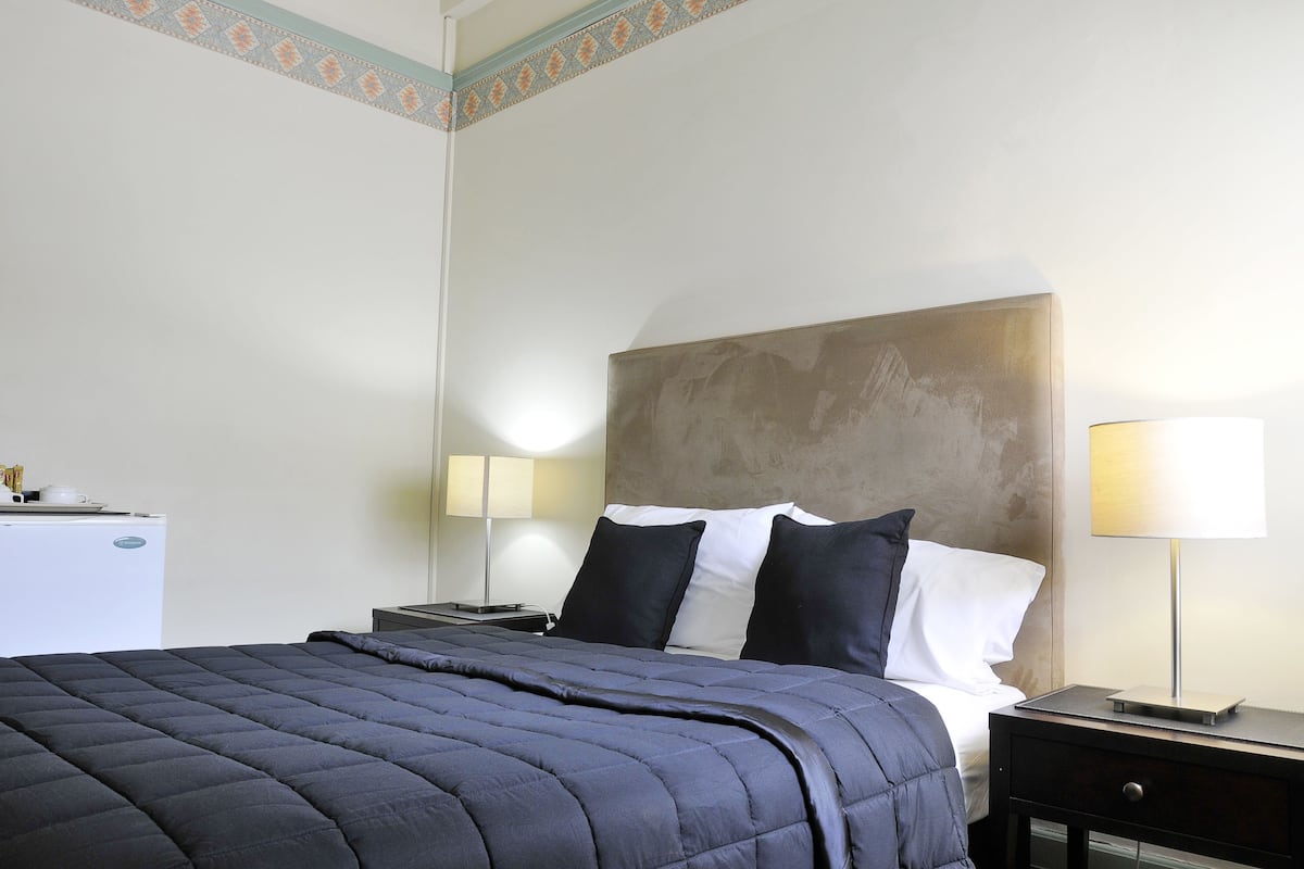 A hotel room with a bed, bedside tables, a lamp, and a small refrigerator.