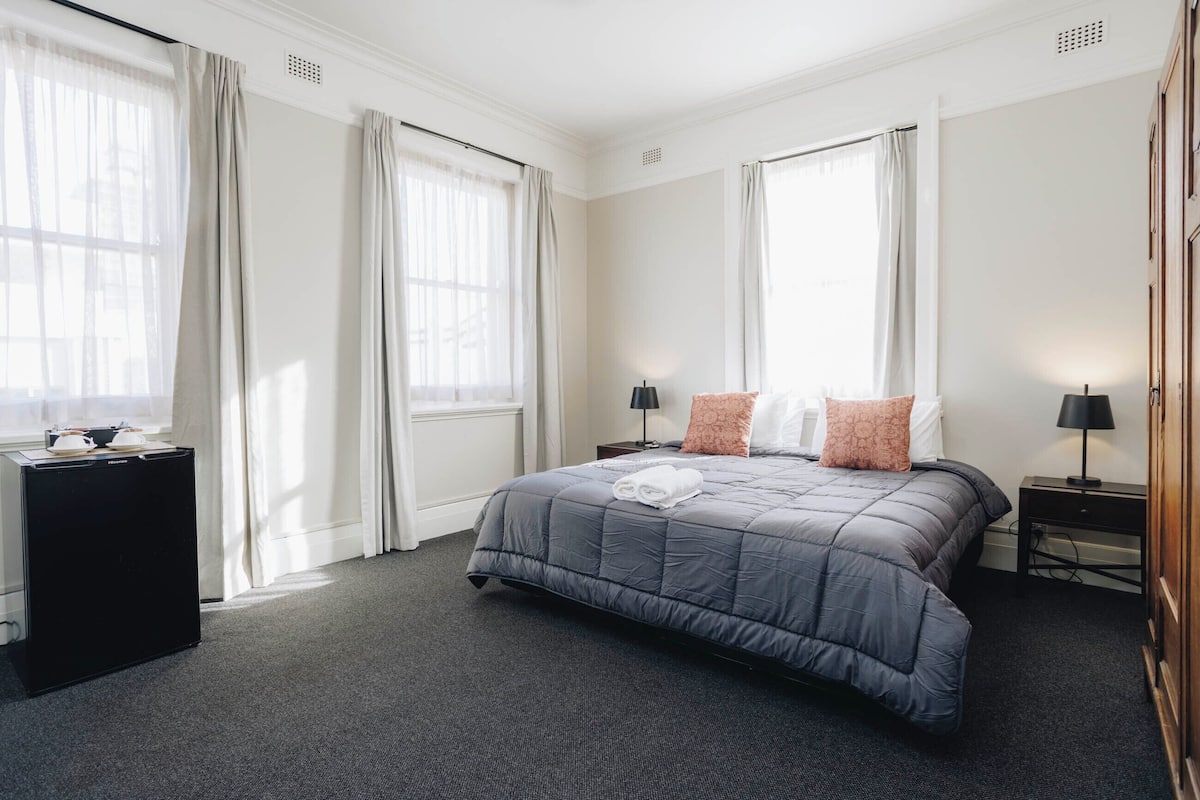 A neatly arranged bedroom with a large bed, two bedside tables with lamps, and a small side table with a lamp.
