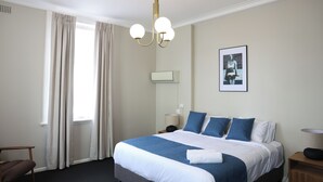 A hotel room with a large bed, a desk, a chair, a lamp, and a picture on the wall. - Hotel Gosford (Gosford)